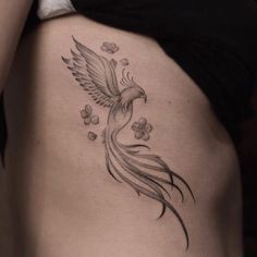 a woman's stomach with a bird and flowers tattoo on her side ribcage