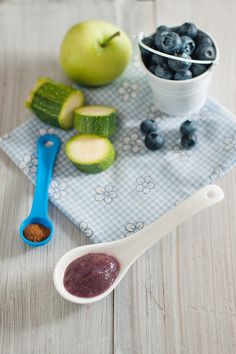 blueberries, apples and cucumbers sit on a towel next to a spoon