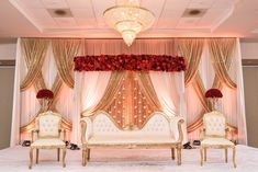 an elaborately decorated stage with two white couches and red flowers on the wall