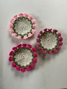 three crocheted baskets with pink and green flowers in them on a white surface