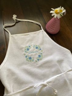 a white apron with blue flowers on it next to a pink vase and wooden floor