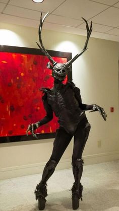 a woman dressed as a creature in front of a large red and black painting on the wall