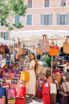 a woman standing in front of an outdoor market with lots of bags and purses