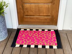 a pink and black door mat sitting on top of a wooden floor next to a brown door