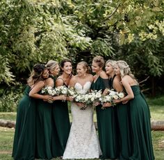 a group of women standing next to each other in front of trees and grass holding bouquets