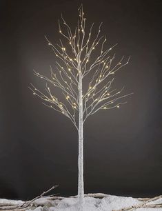 a white tree with lights on it in the middle of snow covered ground, against a dark background