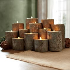 a bunch of lit candles sitting on top of a wooden table next to pine cones