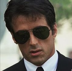 a close up of a person wearing sunglasses and a suit with a tie in the background