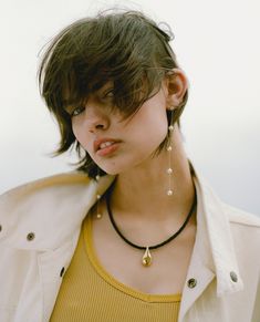 a woman wearing a yellow shirt and black choker with pearls on her necklaces