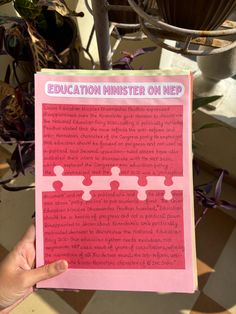 a person holding up a pink book with the words education minister on it