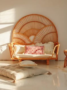 a wicker couch with pillows on the floor in front of a white wall and table