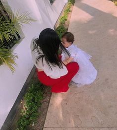 a woman kneeling down next to a baby in a red and white dress on the sidewalk