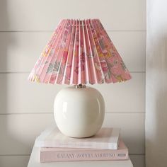 a white lamp sitting on top of a stack of books next to a pink lampshade