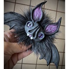 a hand holding a fake bat with purple eyes and black fur on it's head