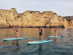 three people on paddle boards paddling in the water near rocky cliffs and cliffs behind them