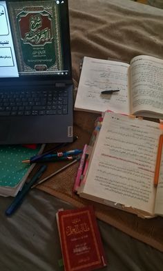 an open book sitting on top of a bed next to a laptop computer and books