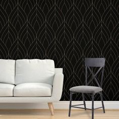 a white couch sitting next to a chair in front of a wall with black designs on it