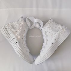 two white sneakers with bows and pearls are on a white sheet that is laying down