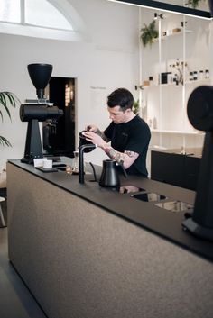 a man standing at a counter in front of a coffee grinder holding a cup