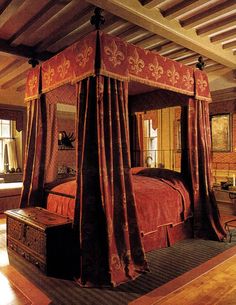 the canopy bed is made up with red sheets and drapes on it's sides