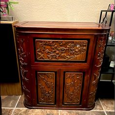 a wooden cabinet sitting on top of a tile floor next to a vase with flowers