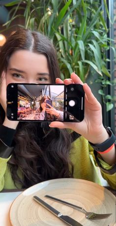 a woman taking a selfie with her cell phone at a table in a restaurant