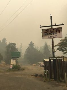 a sign that is on the side of a road in front of some trees and bushes