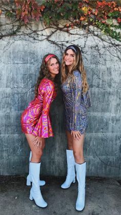 two women standing next to each other in front of a wall with vines on it