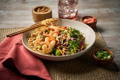 a white bowl filled with noodles and vegetables next to chopsticks on top of a table