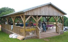 two people standing on the porch of a wooden gazebo with picnic tables in the background