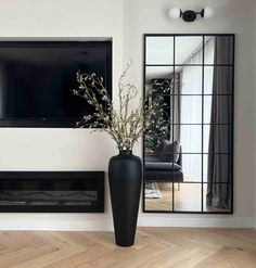 a large black vase with flowers in it sitting next to a mirror on the wall