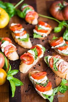 small sandwiches with tomatoes and basil on a wooden cutting board next to some fresh vegetables