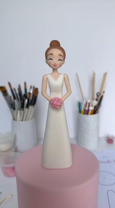 a cake with a bride figurine on top of it next to paintbrushes