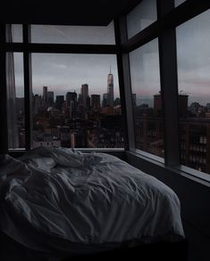 an unmade bed in a room with large windows overlooking the cityscape and skyscrapers