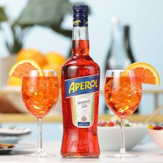 a bottle of aperol next to two wine glasses filled with orange slices and garnishes