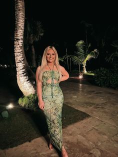 a woman in a green dress standing next to a palm tree at night with her hands on her hips