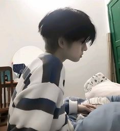 a young man sitting on top of a bed next to a green dresser and mirror