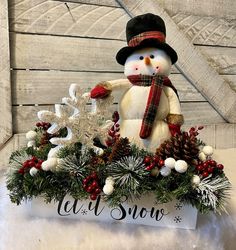 a snowman sitting on top of a box filled with pine cones and other decorations