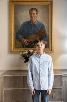 a young boy stands in front of a portrait of a man with a dog on his chest