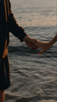 two people holding hands in the water at sunset or sunrise, with one person reaching out to another person's hand