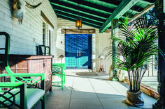 a porch with chairs and a potted plant on the side walk next to a blue door