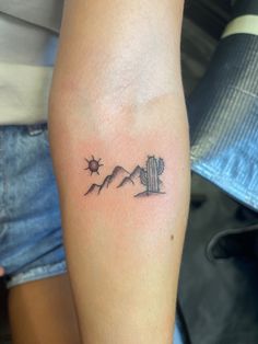 a small cactus and mountains tattoo on the left arm, with stars in the sky