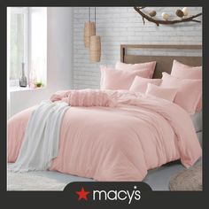 a bed with pink comforters and pillows in a white brick wall bedroom, next to a window that reads macy's