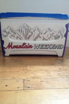 a cooler sitting on top of a wooden floor in front of a wall with the words mountain weekend written on it