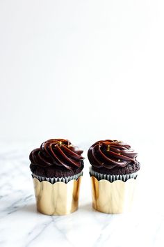 two cupcakes with chocolate frosting and sprinkles sitting on a marble surface