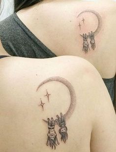 two women with tattoos on their backs are holding hands up to the moon and stars