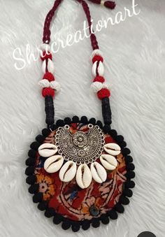 a red and white necklace with shells on it's end, hanging from a black cord