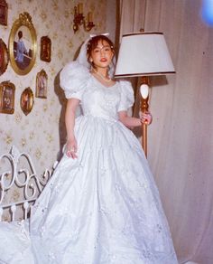 a woman in a white wedding dress standing on a bed with a lamp next to her