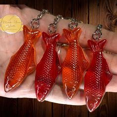 four red fish shaped glass key chains on a person's hand