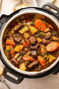 a pot filled with stew and carrots on top of a white tablecloth next to bread